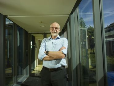 Andrew Pollard: a white man wearing a blue shirt, standing in a walkway with windows on each side