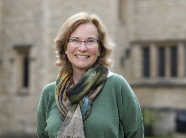 Portrait photograph of Professor Helena Hamerow, a white lady with shoulder length light brown hair and glasses. She stands outside University of Oxford College buildings.