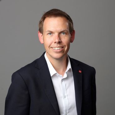 Professor Paul Shearing, a white man with short brown hair, wearing a black suit and white shirt. He stands in front of a plain grey background.