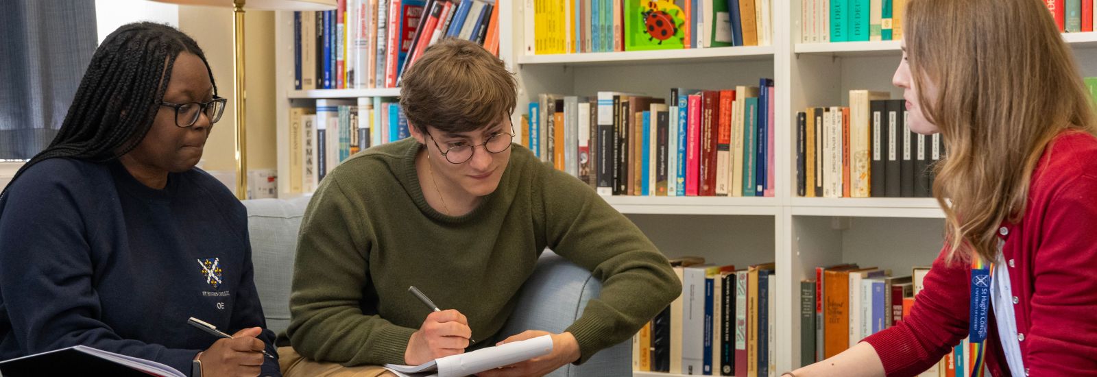 Two students are sitting making notes. Books surround them.