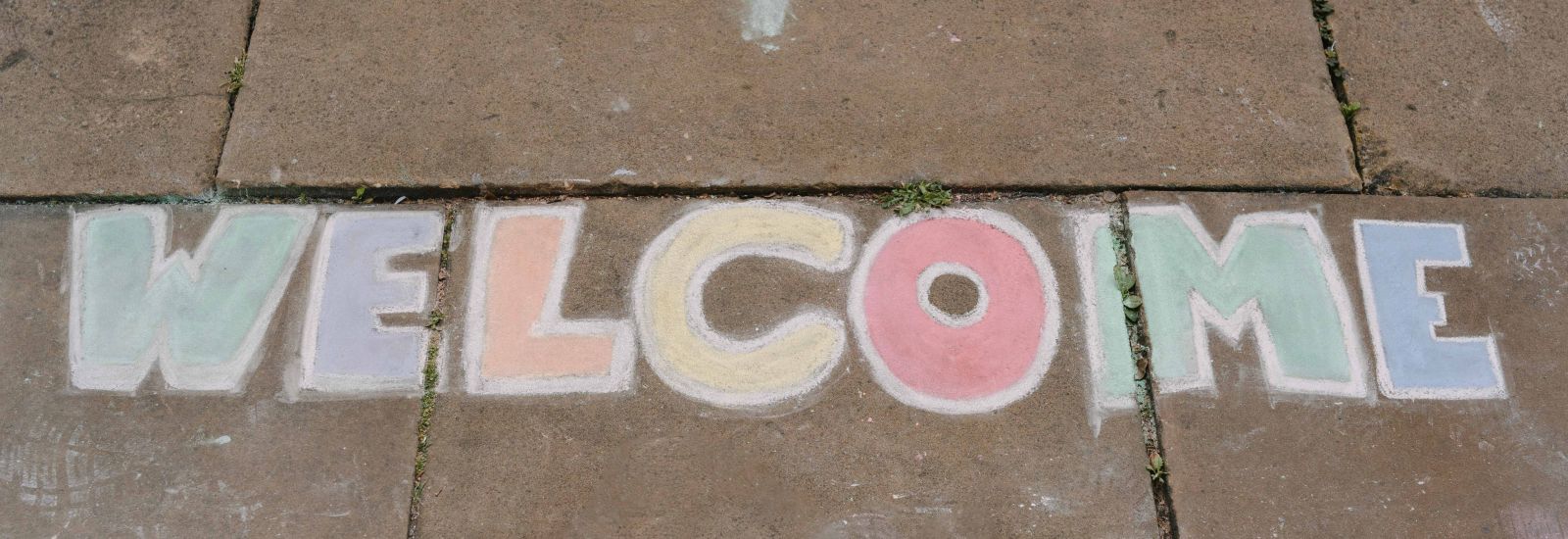 The word 'Welcome' written in chalk on some paving stones.