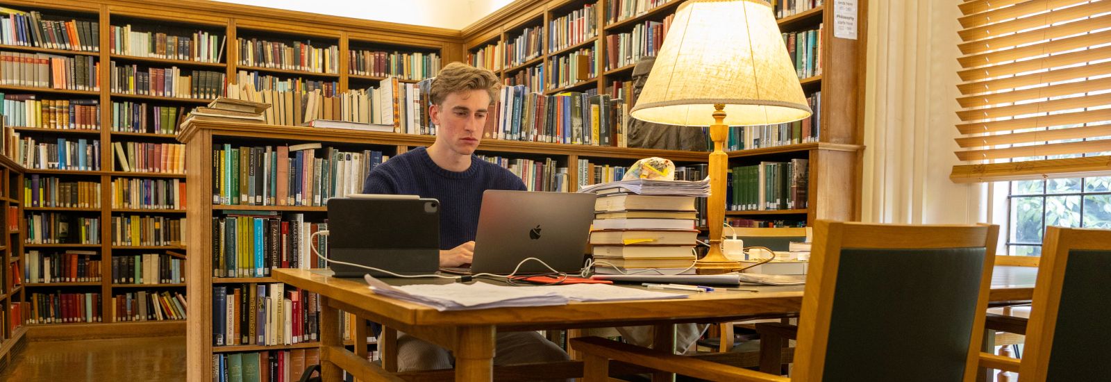 A student studies in the Balliol College library, surrounded by bookshelves and typing on a laptop. 