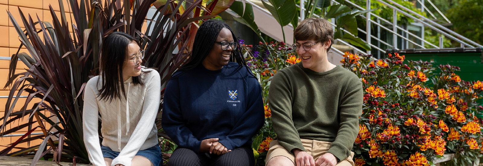 Three students sitting on a bench laughing together