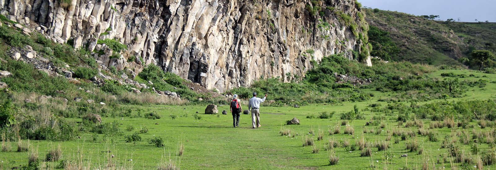 Two people walking outside in grassland with a cliff to the left