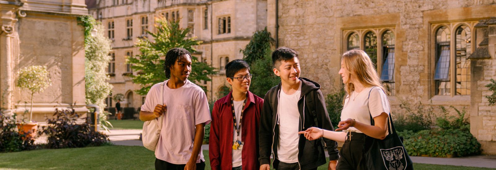 Four students are talking to one another and smiling as they walk between the buildings of an Oxford college.