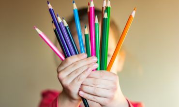 Image of a child holding up a selection of colouring pencils in front of the camera
