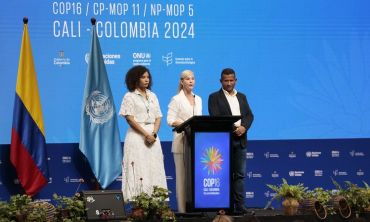 Two women and a man of mixed nationalities stand at a podium in front of a banner for the United Nations Conference of the Parties for Biodiversity (COP16), banner for the 