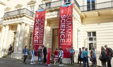Queues of people outside the entrance to The Royal Society’s headquarters in London. The entrance is flanked by two large red banners which each say ‘Summer Science Exhibition.’