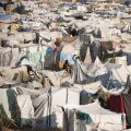 A crowded scene of makeshift tents clustered close together in a barren landscape. 