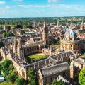 Aerial view of historical Oxford University buildings built in yellow stone, including All Souls College, the Bodleian Library and the Radcliffe Camera (a circular building with a dome). 