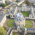 Aerial view of historical Oxford University buildings built in yellow stone, including All Souls College, the Bodleian Library and the Radcliffe Camera (a circular building with a dome). 