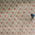 Looking down at a man on his own looking at his phone stood alone in a large tiled room